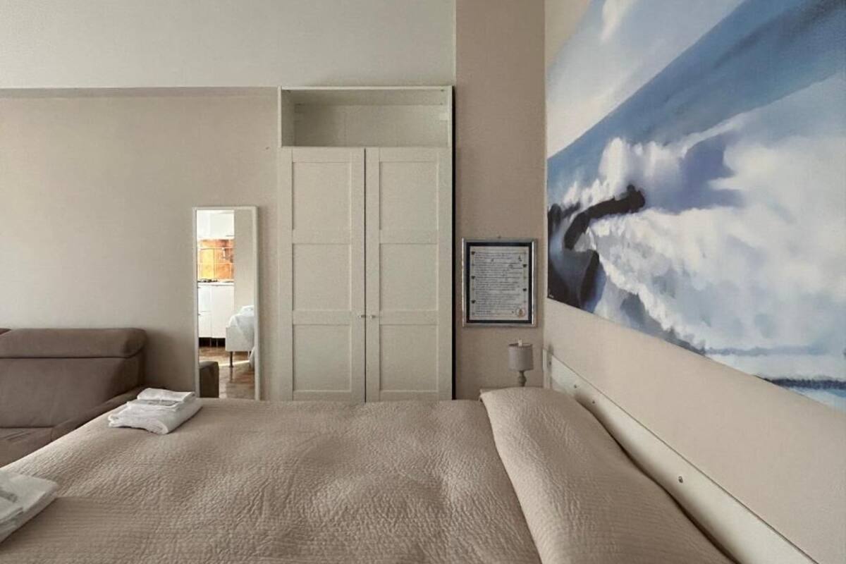 A hotel room with a large bed, a painting of clouds on the wall, and a view into the bathroom.