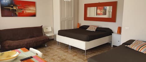 A bedroom with a bed, a sofa, a small table with a bowl and remote, and a mirror on the wall.
