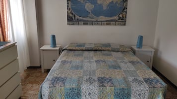 Une chambre avec une grande carte du monde accrochée au mur, deux tables de chevet ornées de vases, un lit recouvert d’une courtepointe à motifs et une commode à tiroirs.