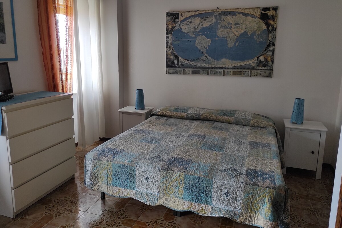 A bedroom with a bed, a dresser, a nightstand, a map on the wall, and a television on the dresser.