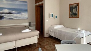 A hotel room with two beds, a painting of a beach scene, a small table, and a chair.