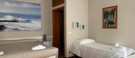 A hotel room with two beds, a painting of a beach scene, a small table, and a chair.
