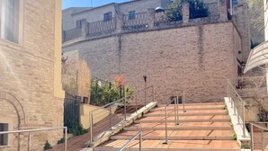A paved area with steps leading up to a brick wall, metal railings, and a building with a window. - Monolocali Da Vinci (Falconara Marittima)