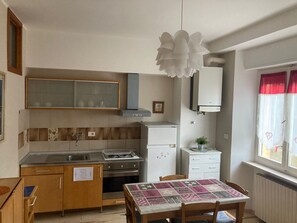 Cocina compacta con estufa a gas, horno y refrigerador pequeño. Cuenta con una mesa de comedor con mantel estampado y sillas.