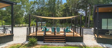 A deck with outdoor seating and a canopy, surrounded by trees.
