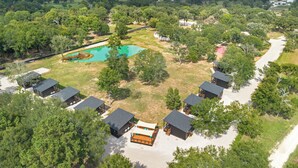 Vista aérea de un complejo turístico con varias cabañas, una piscina y abundante vegetación.