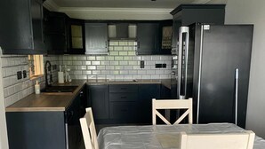 A modern kitchen with dark cabinets, a stainless steel refrigerator, and a dining area with a table and chairs.