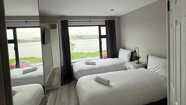 A hotel room with two beds, a large window with a view of a body of water, and a mirror reflecting the room.