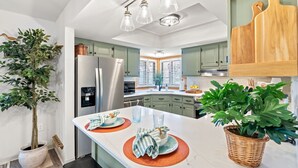 A modern kitchen with a central island, stainless steel appliances, and green cabinets.
