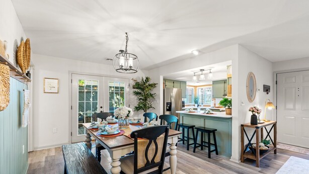 A spacious dining area with a wooden table, chairs, and a bench. There is a kitchen visible in the background with a large island and bar stools.