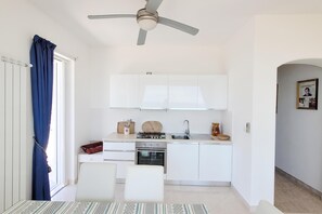 Una cocina compacta con armarios blancos, estufa a gas, un lavamanos y ventilador de techo.