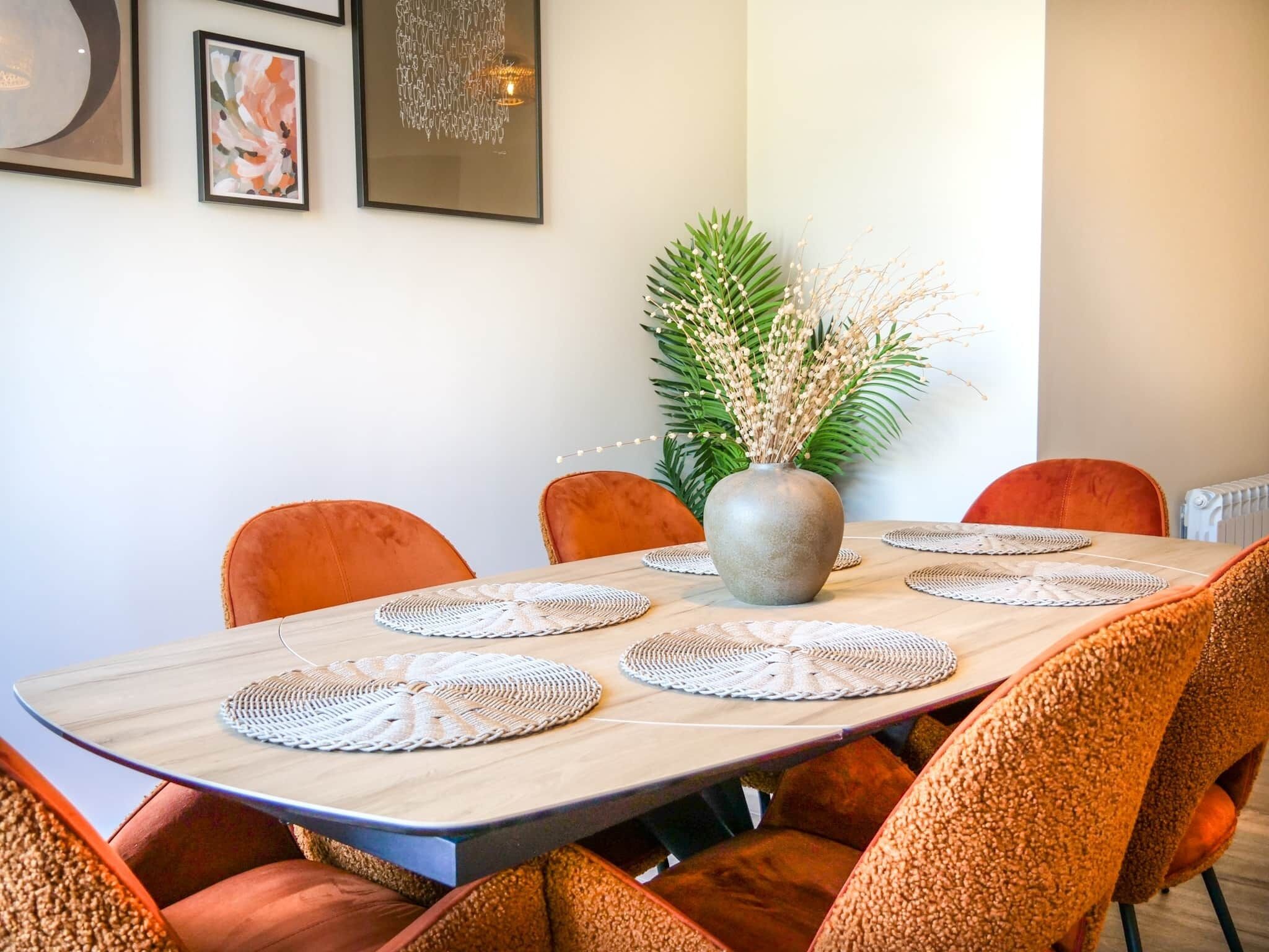 Una mesa de comedor con individuales tejidos, rodeada de sillas tapizadas en color naranja.
