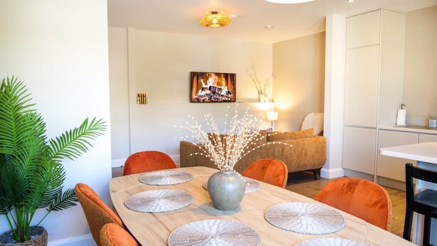 Un coin repas avec une table en bois, des chaises orange et un vase décoré de branches.
