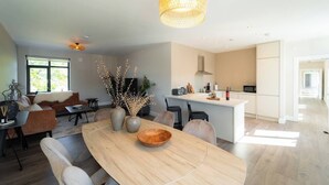 Une cuisine moderne avec un îlot central, un coin repas doté d’une table en bois et un salon avec un canapé et un téléviseur.