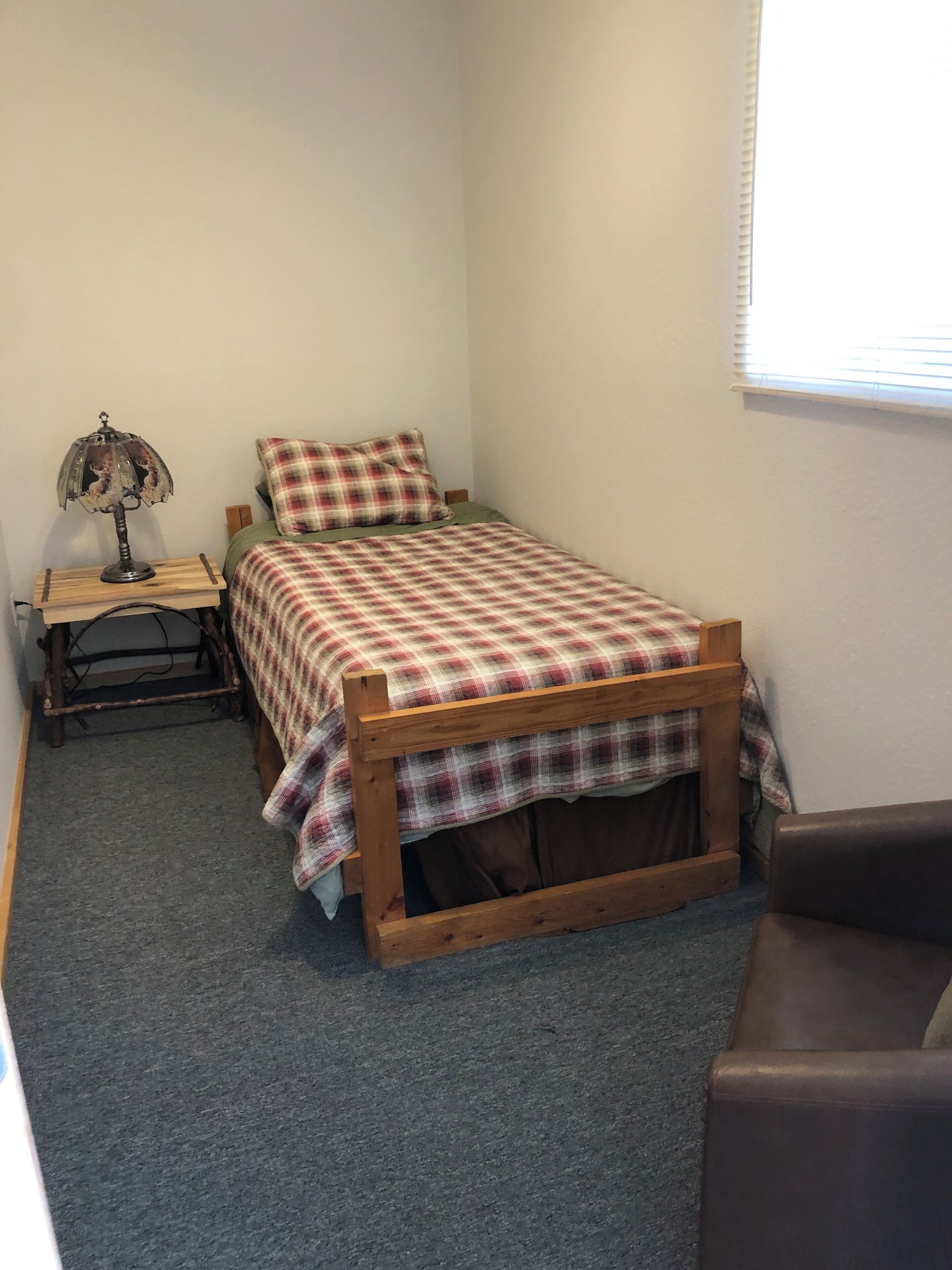Un dormitorio pequeño y ordenado con una cama individual, una mesita de noche, una lámpara y una ventana.