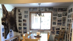 Ein Esszimmer mit einem großen Holztisch, Stühlen, einer Bank, einem aufgehängten Tierfell und einer Wand voller gerahmter Bilder.