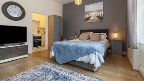 A bedroom with a bed, bedside tables, a TV, a clock, and a painting on the wall.