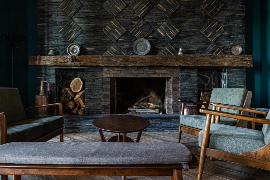 A cozy living room with a fireplace, wooden furniture, and a patterned wall.