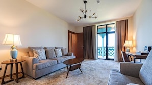A hotel room with a sofa, a coffee table, a lamp, a dining table, and a view through a large window. - Agarani Estate (Telavi)