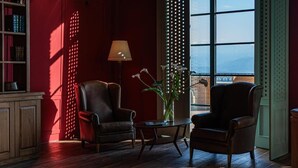 A room with two leather armchairs, a small table, a lamp, and a view through a large window. - Agarani Estate (Telavi)
