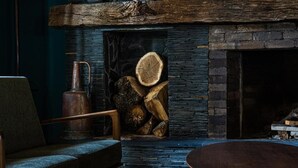 A cozy room with a stone fireplace, a rustic wooden mantel, and a seating area with a chair and a round table. - Agarani Estate (Telavi)