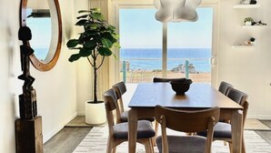A dining area with a wooden table and chairs, a large mirror, a potted plant, and a view of the sea through a large window.