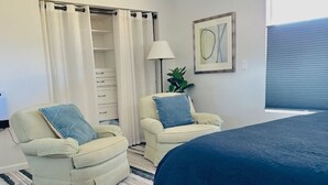 A bedroom with a bed, two chairs, a lamp, a plant, and a closet.