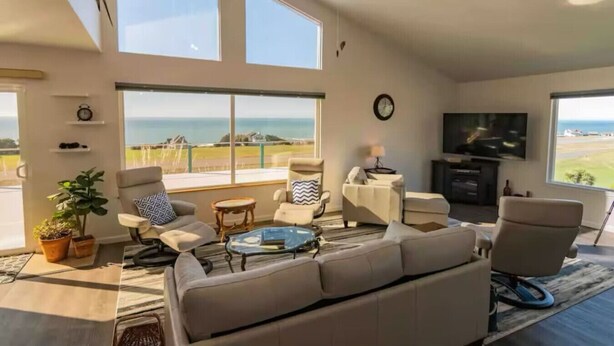 A spacious living room with a large window offering a view of the sea, a flat-screen TV, and a comfortable seating area with a sofa and chairs.