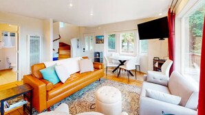 A modern living room with a leather sofa, a white armchair, and a dining area with a table and chairs. - Stunning Ocean View Getaway- Private and Serene (Whitethorn)