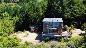 A two-story cabin with a deck, surrounded by dense forest. - Stunning Ocean View Getaway- Private and Serene (Whitethorn)