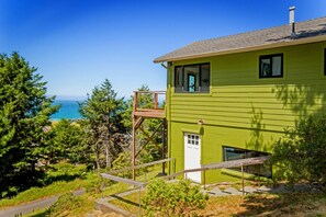 A green house with a wooden deck and a view of the ocean. - Sea Escape at Spruce Overlook (Whitethorn)