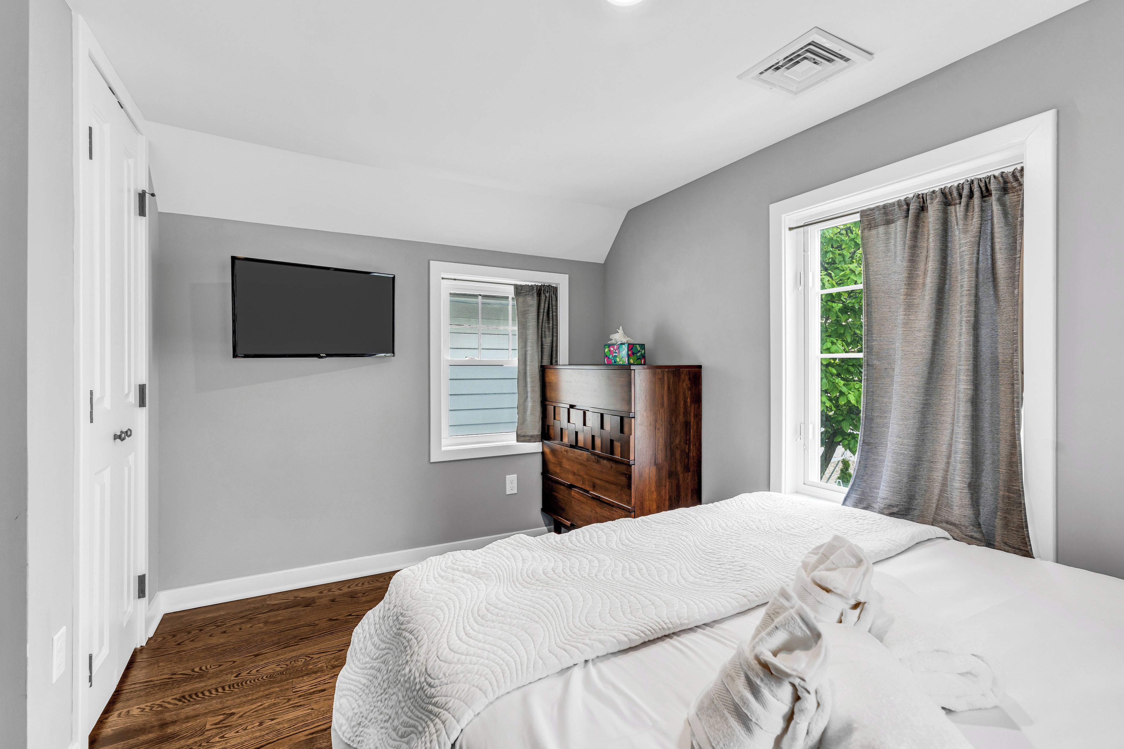 A bedroom with a bed, a dresser, a television, and a window with curtains.