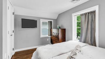 A bedroom with a bed, a dresser, a television, and a window with curtains.