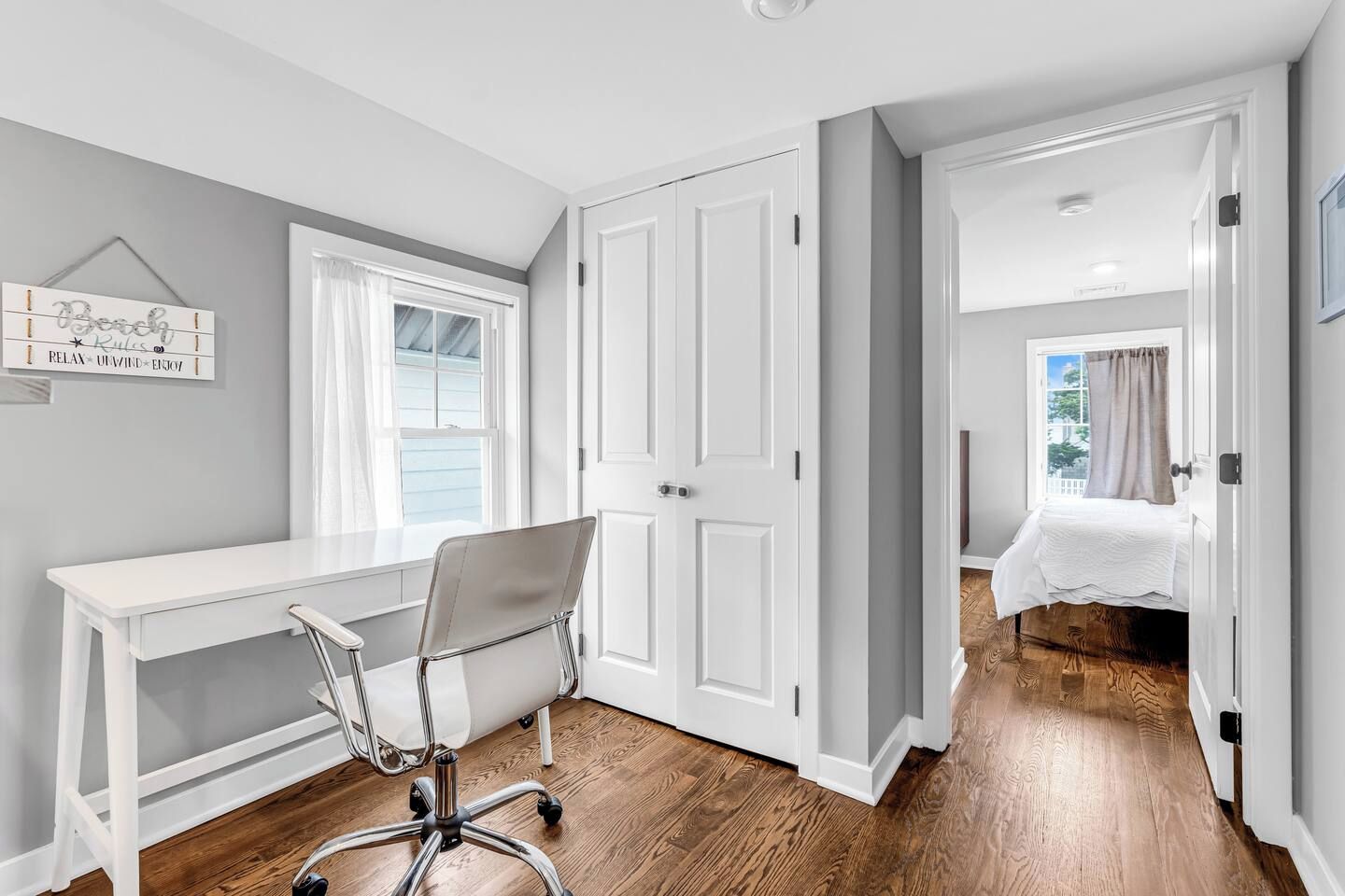 Una habitación con escritorio blanco, una silla, armario grande y cama con vista al exterior.