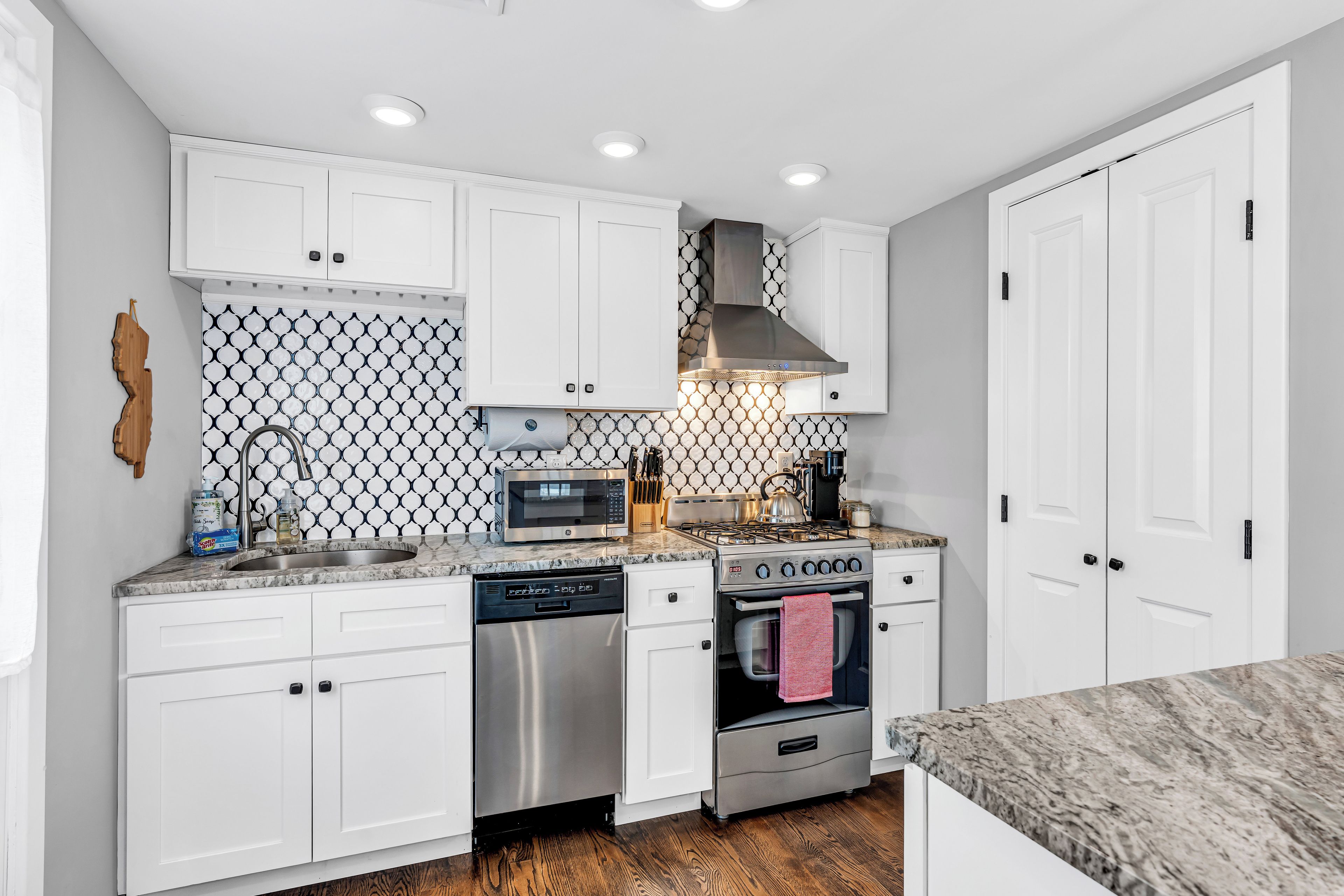 A modern kitchen with white cabinets, a stainless steel dishwasher, a stove, and a microwave.
