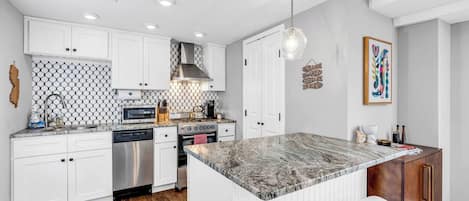 A modern kitchen with white cabinetry, a marble island, and a dining area with white chairs.