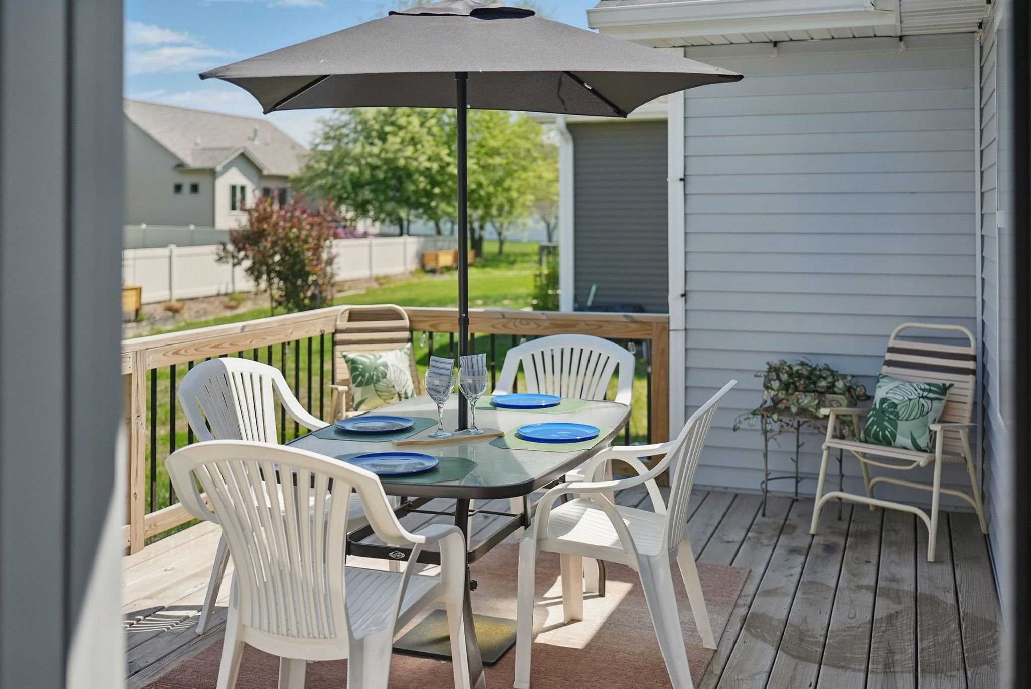 A patio with a table set for two, white chairs, and a large umbrella.