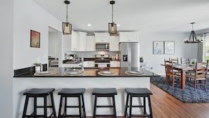 A modern kitchen with white cabinets, a central island with bar stools, and a dining area with wooden chairs and a table.