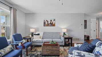 A living room with a grey sofa, blue armchairs, a coffee table, and a painting of cows on the wall.