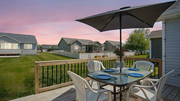 A deck with a table and chairs, surrounded by a wooden deck and a white railing.