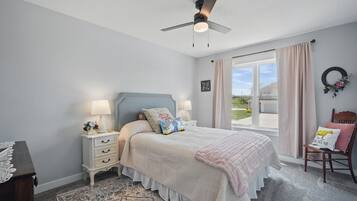 Un dormitorio con cama, mesitas de noche, una silla, ventilador de techo y ventana con cortinas.