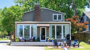 A two-story house with a covered porch, large windows, and a brick chimney.
