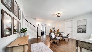 A spacious living area with a wooden floor, a large rug, and a seating area with chairs and a table.