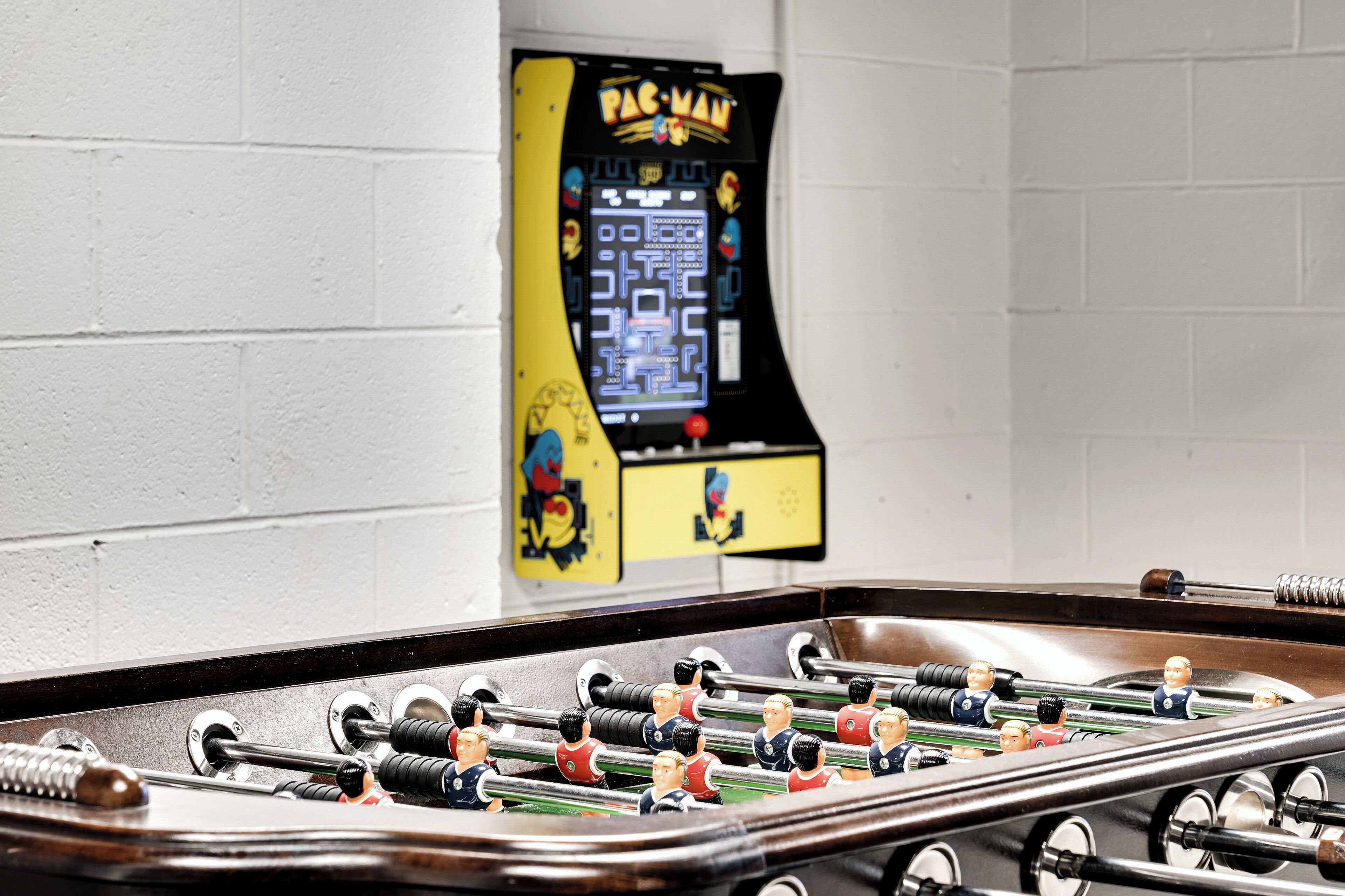 A foosball table with a Pac-Man arcade game in the background.