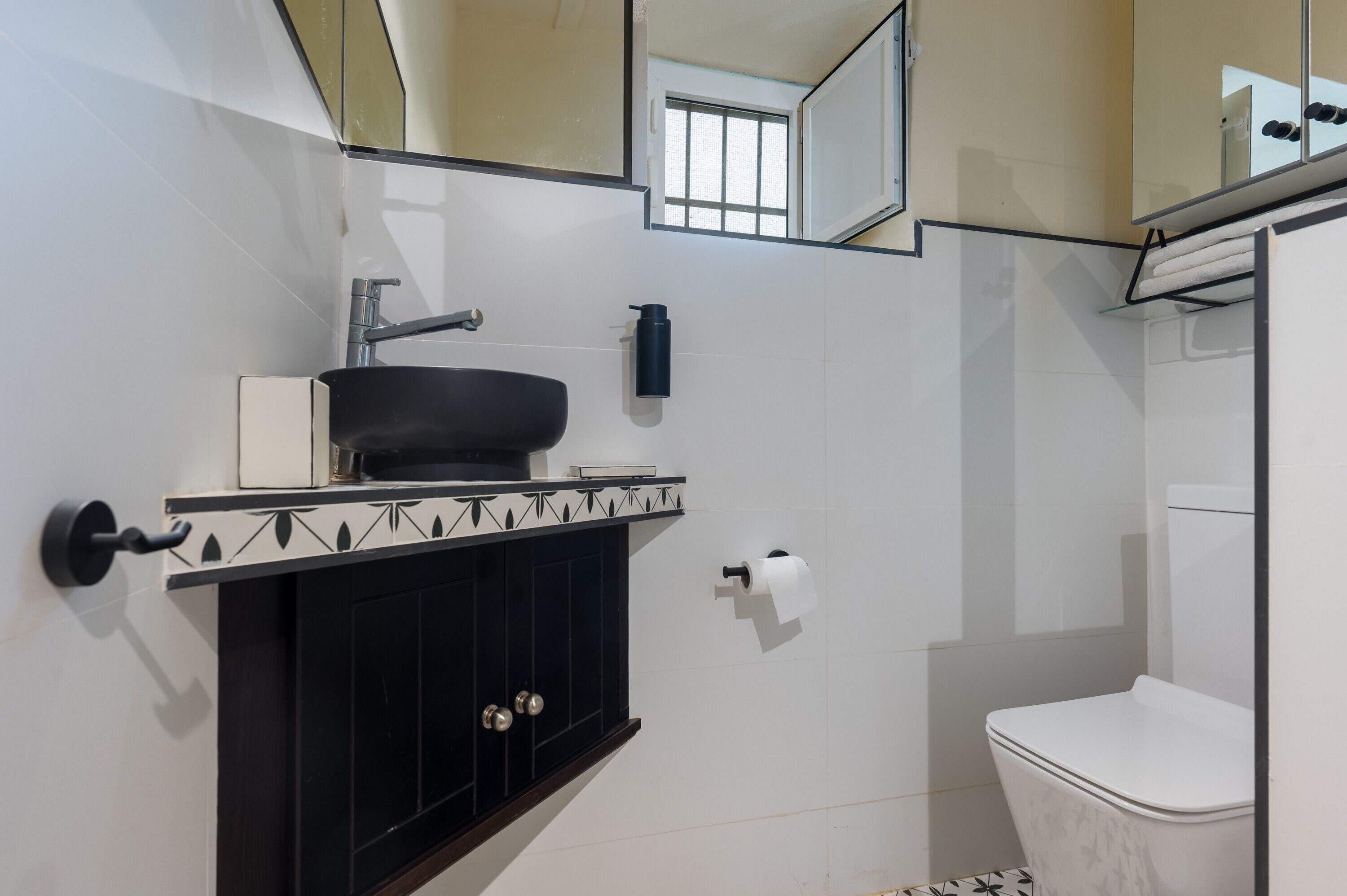 Un baño con un lavamanos negro, inodoro blanco y un espejo sobre el lavamanos.