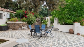 Une terrasse avec un sol carrelé à motifs, une table entourée de chaises et un mur de pierre orné de plantes.
