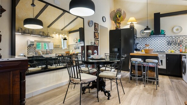 Une cuisine moderne avec un coin repas, comprenant une table ronde avec des chaises, un grand miroir et des luminaires suspendus.