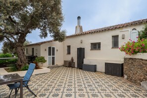 Un patio con suelo de baldosas, una silla, una mesa, una planta en maceta y un edificio con chimenea.