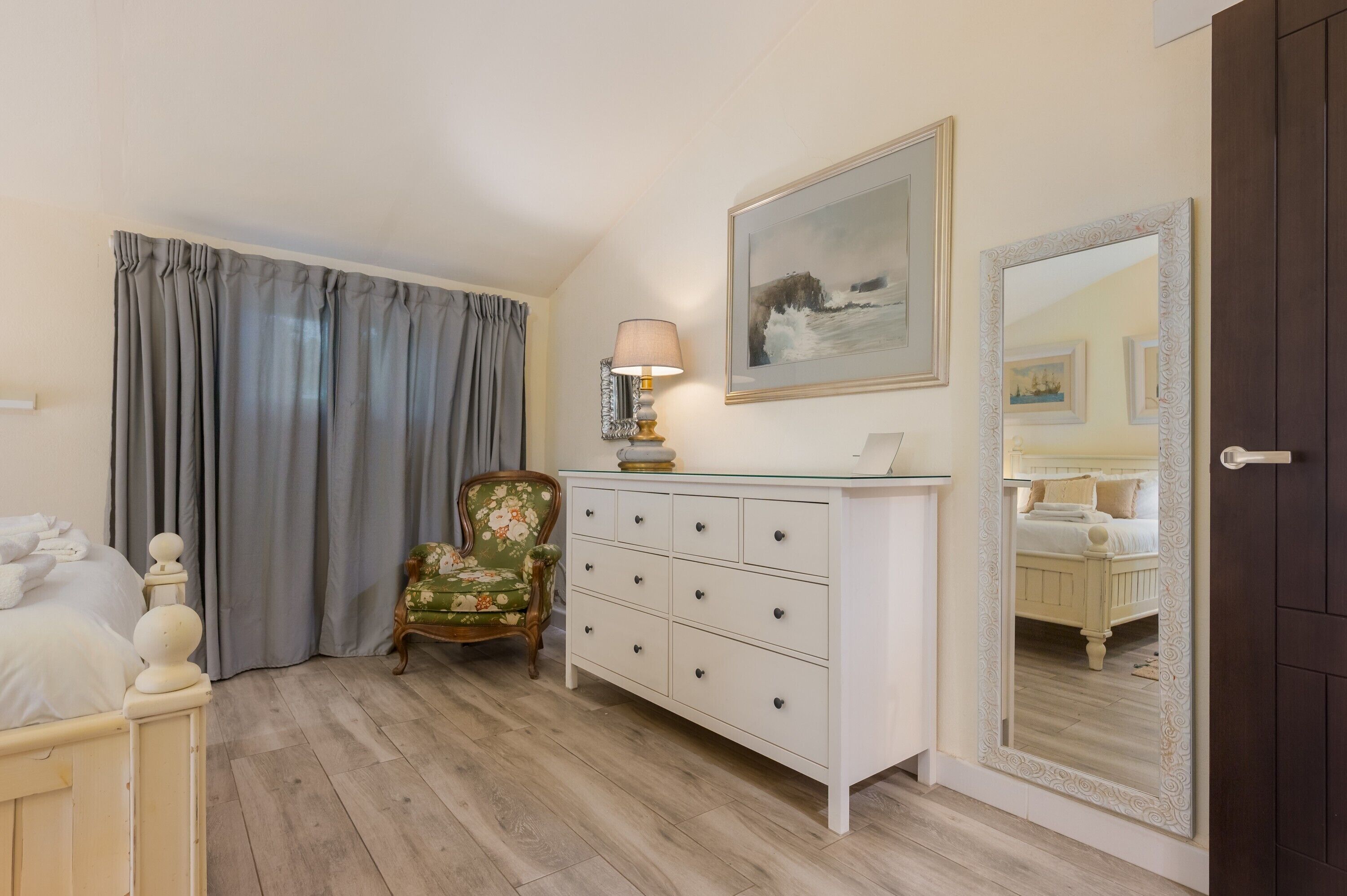 Une chambre à coucher avec un lit, une commode, une chaise, une lampe, un tableau et un miroir.