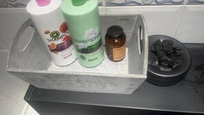 Ein Badezimmerschrank mit einer Shampooflasche, einer Conditionerflasche, einem kleinen Tiegel und einer Schale Holzkohle.